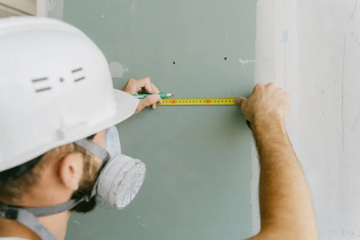 Construction worker measuring drywall during a finishing project