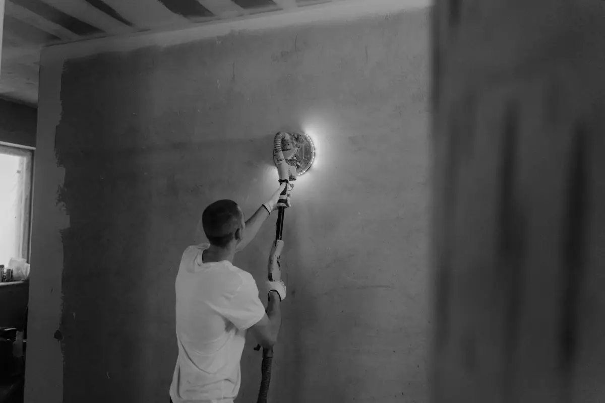 Worker using a power sander on a drywall finish