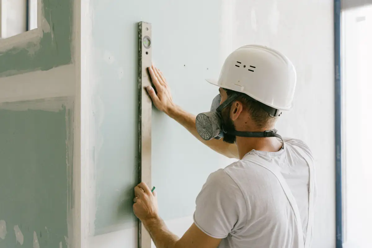 Construction worker using a level to check wall accuracy during drywall installation