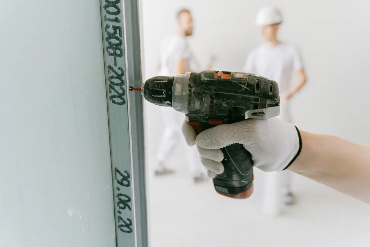 Construction worker using a drill to fasten drywall to framing