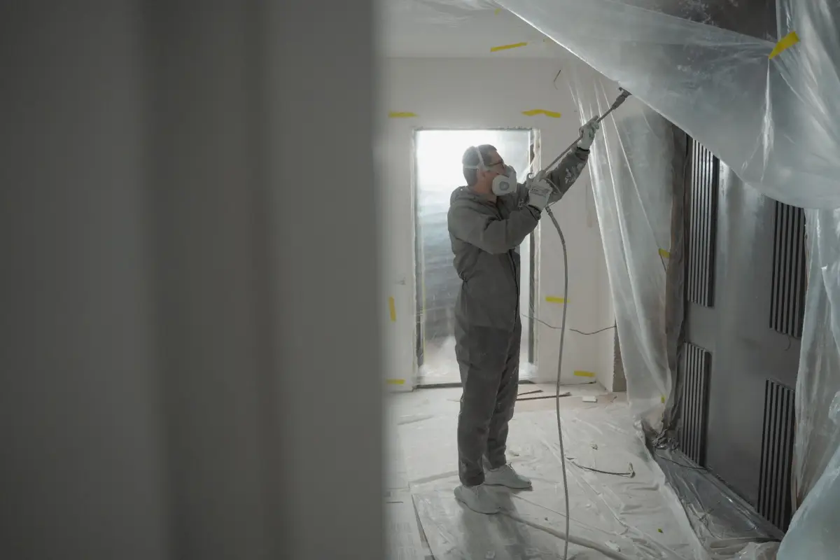 Worker in protective gear applying spray texture to an interior wall